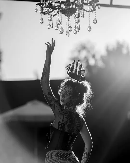 A dancer reaches up beneath a crystal chandelier in evening backlight.
